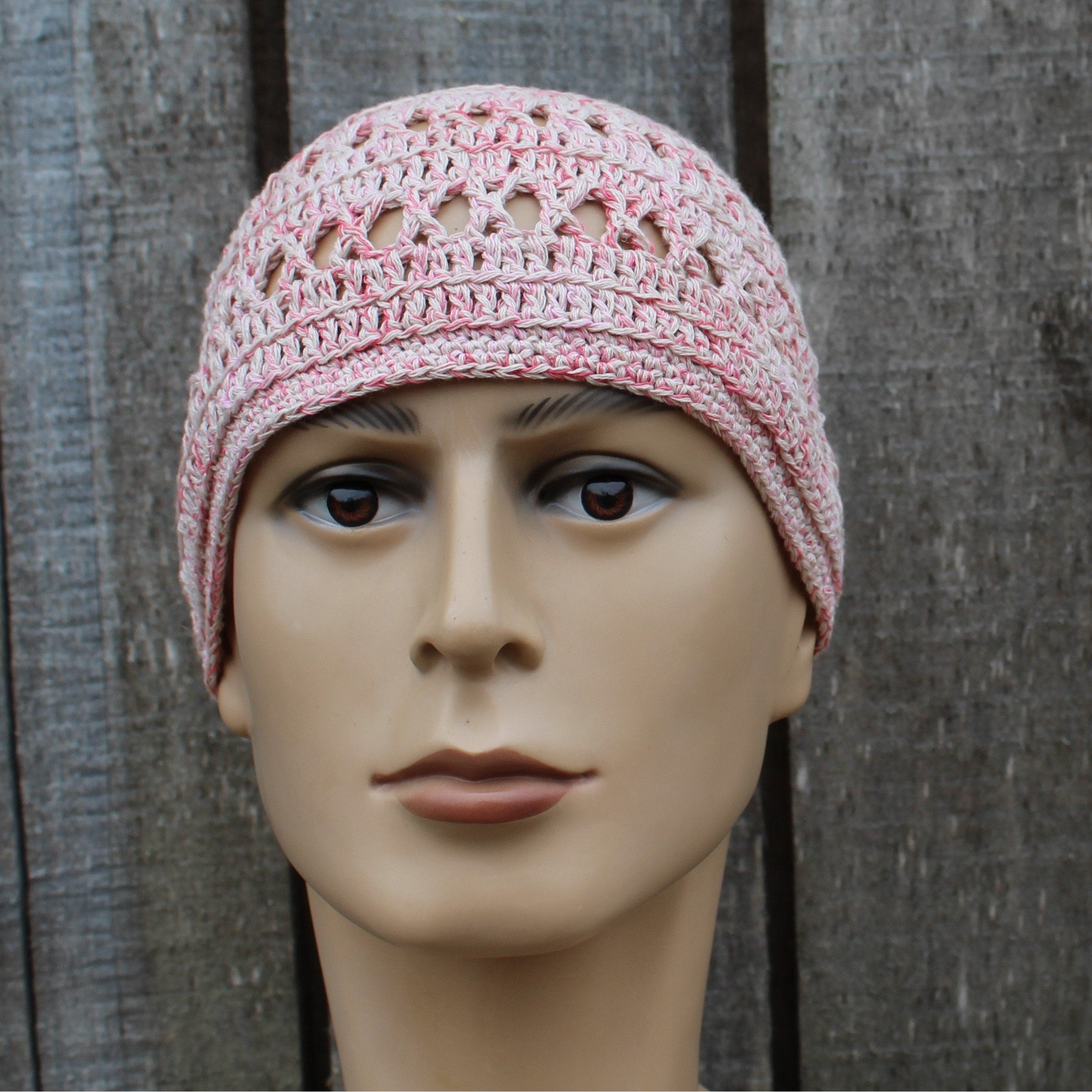 Pink crochet hat on a mannequin head against a wooden background