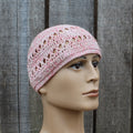 Pink crochet hat on a mannequin head against a wooden background