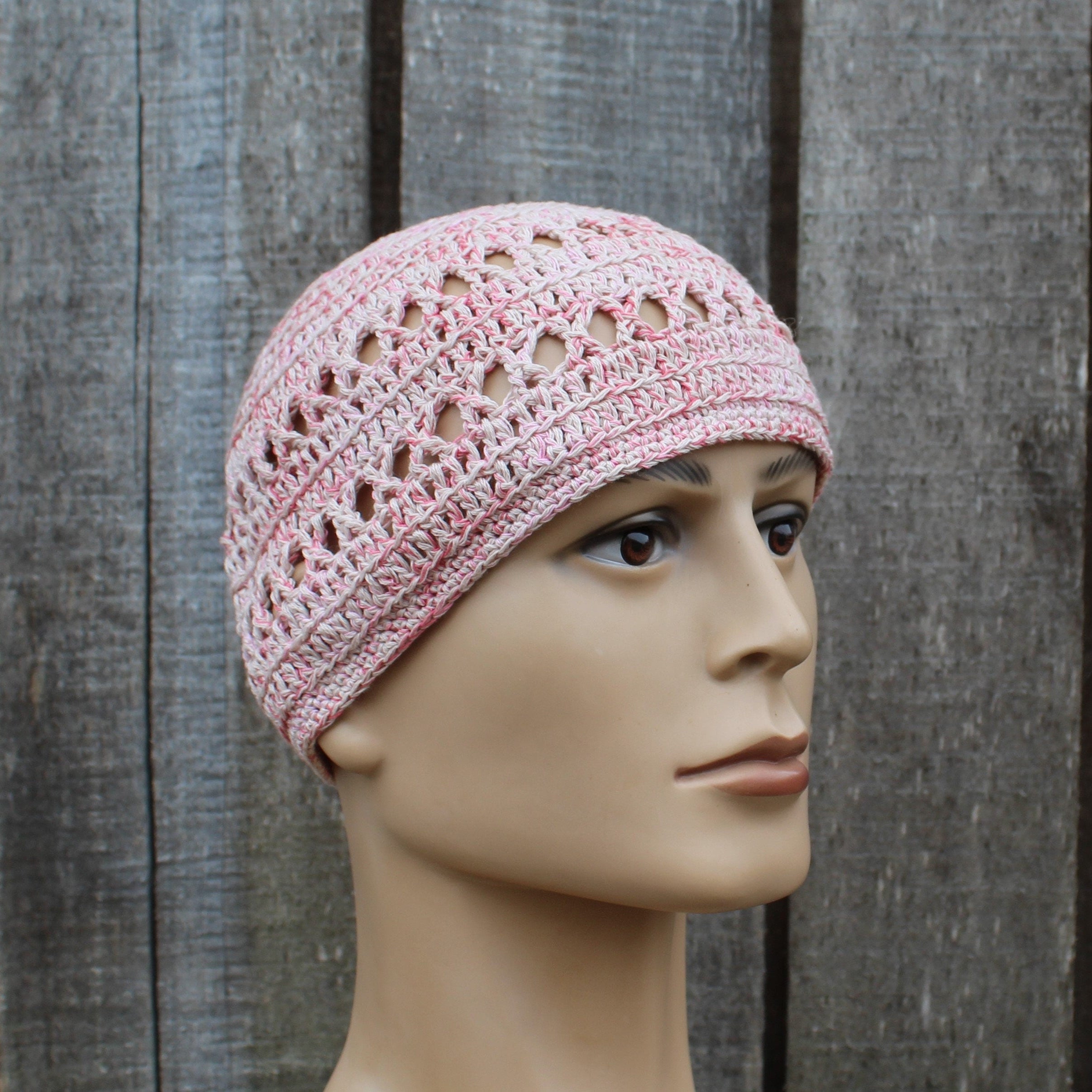 Pink crochet hat on a mannequin head against a wooden background