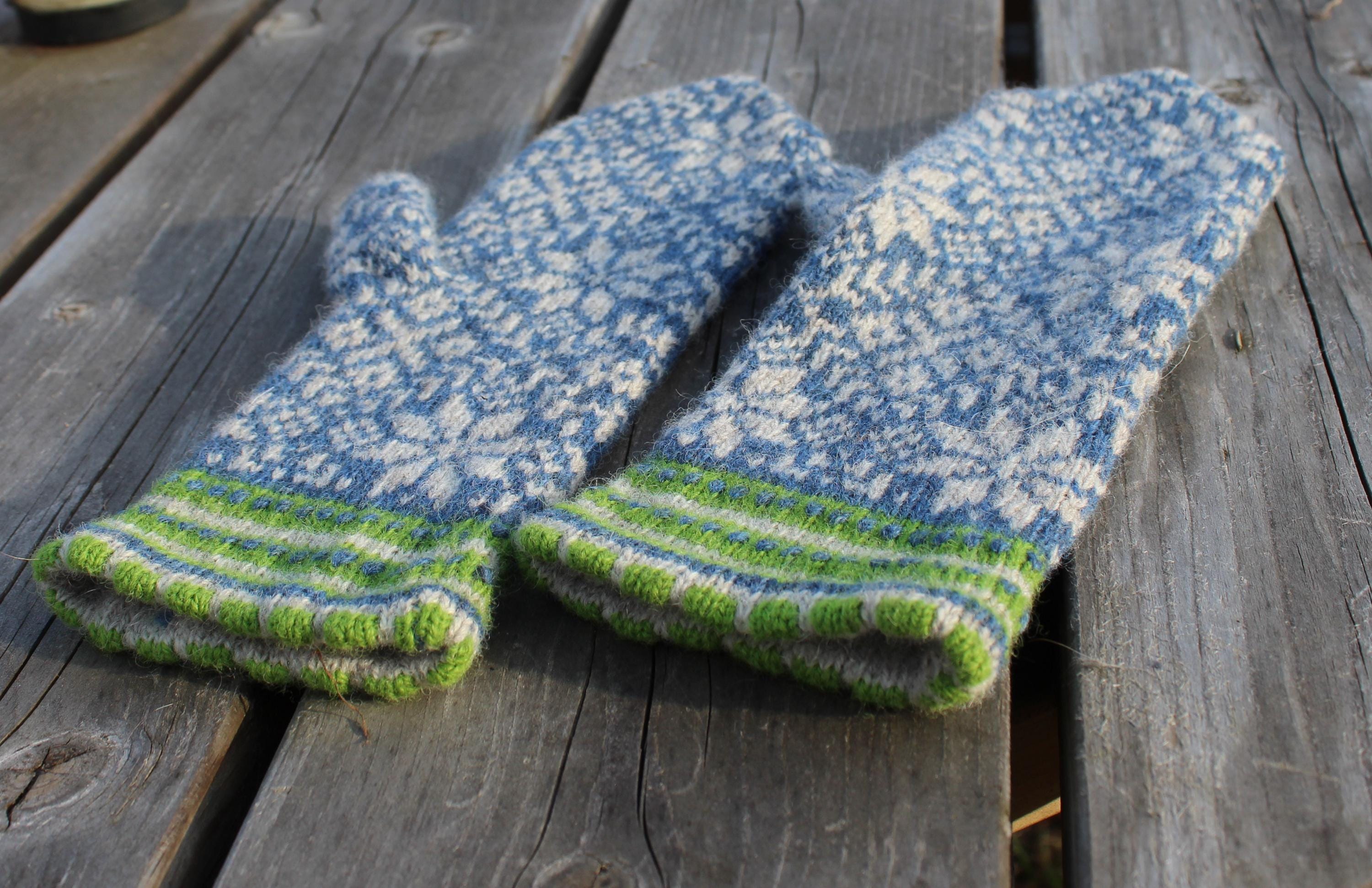Pair of blue and white knitted mittens with green cuffs on a wooden surface
