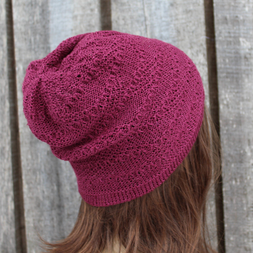 Pink knitted beanie worn by a person against a wooden fence background