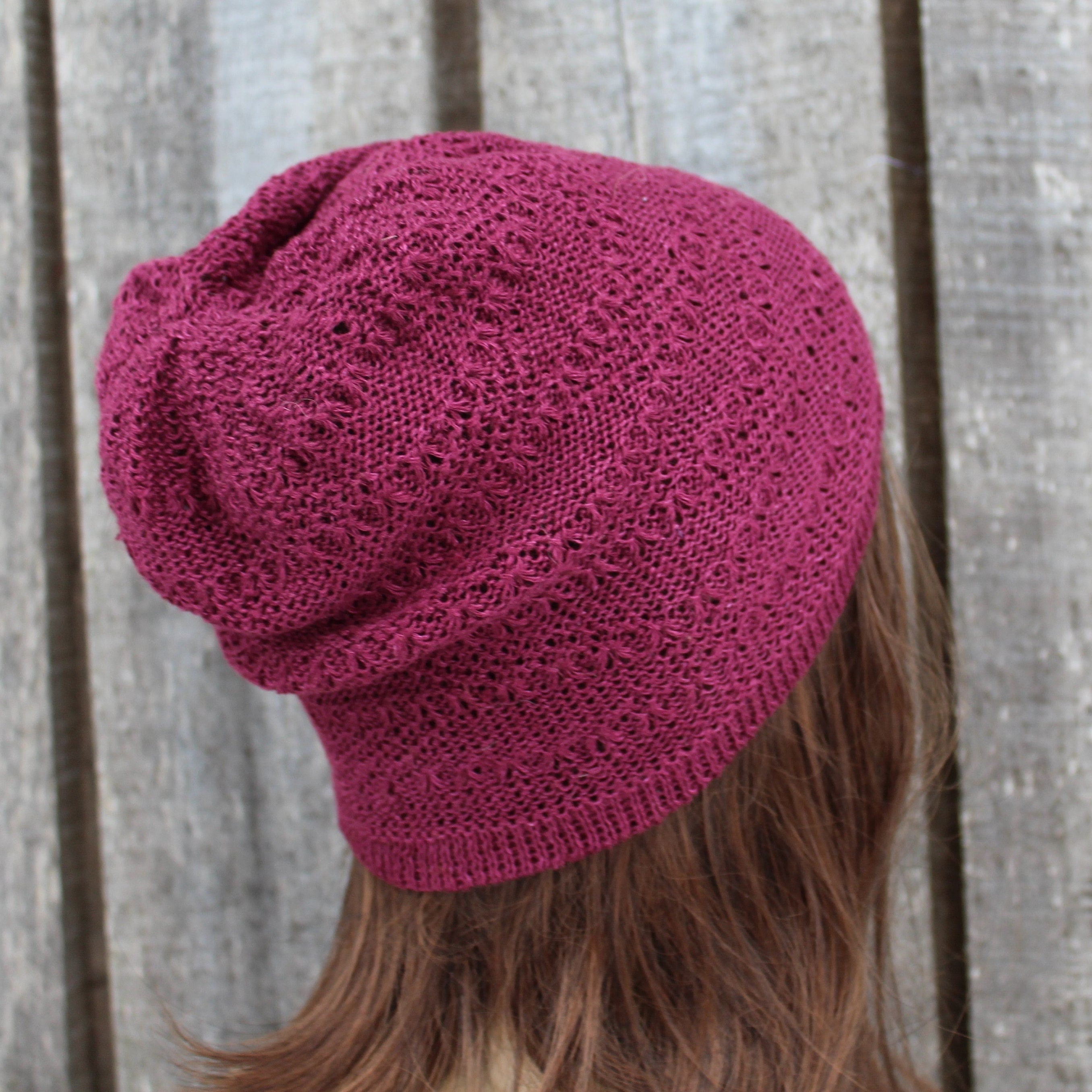 Pink knitted beanie worn by a person against a wooden fence background