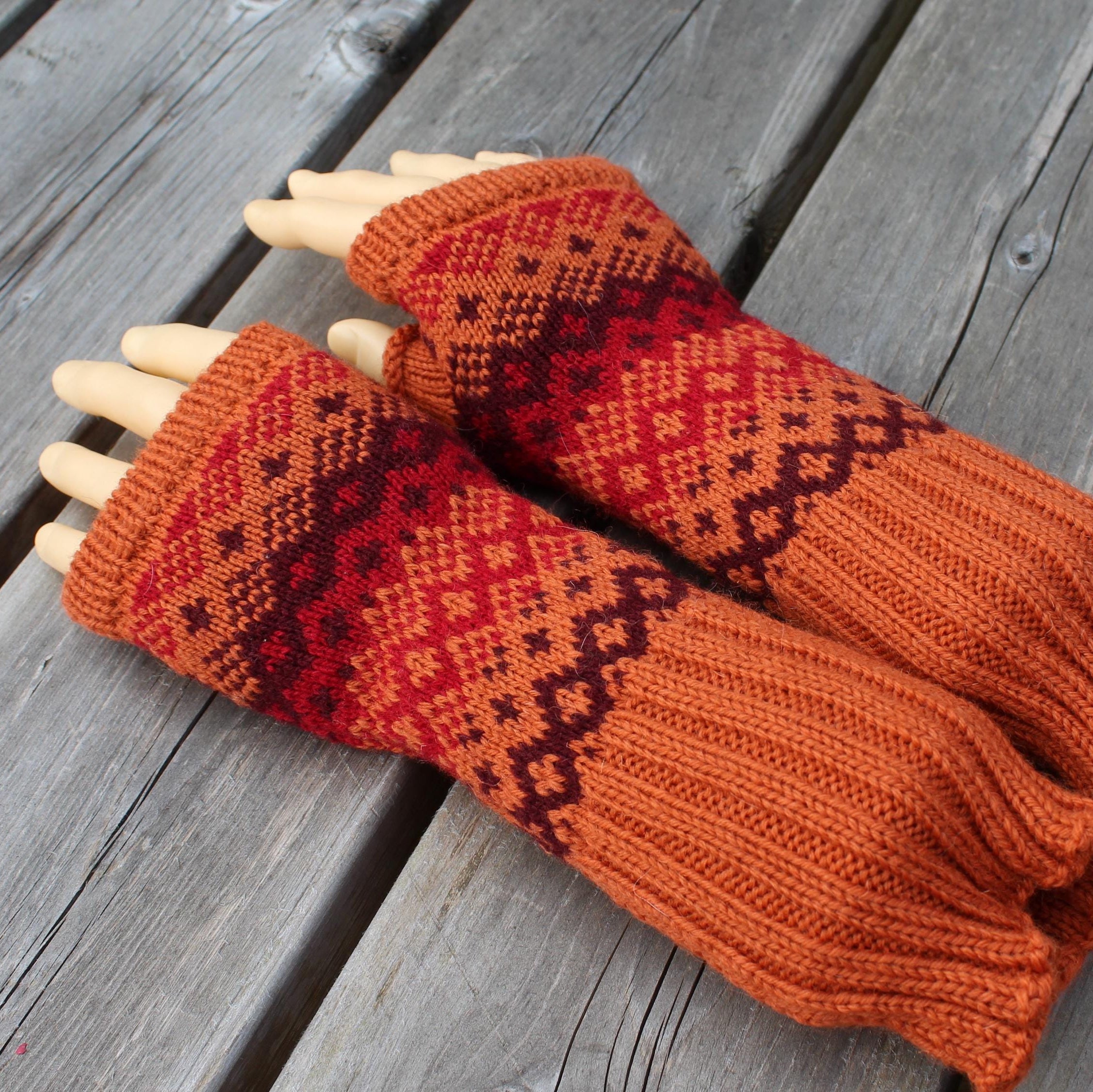 Pair of orange and red patterned fingerless gloves on a wooden surface