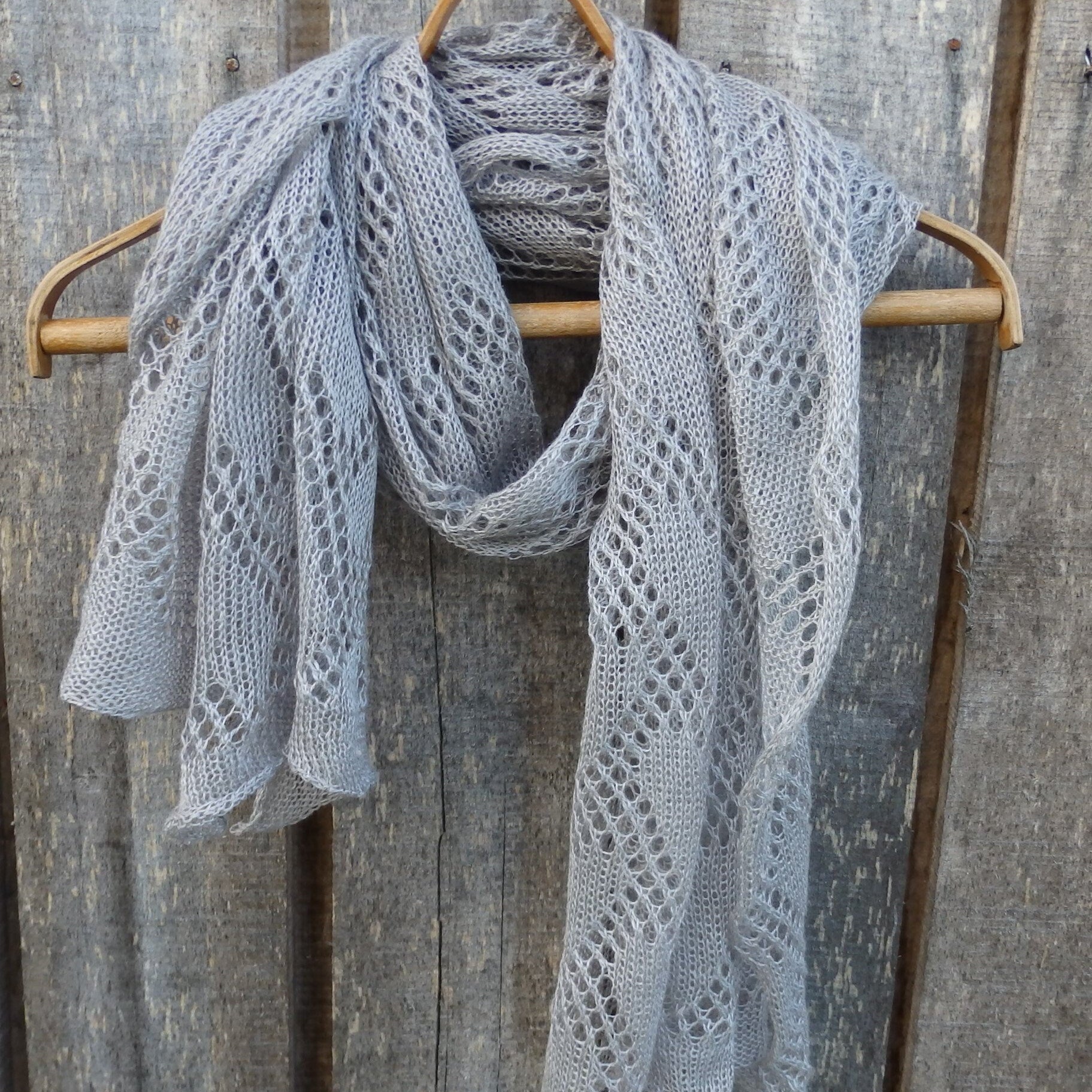  Knitted flax shawl draped over a wooden hanger against a rustic wooden background