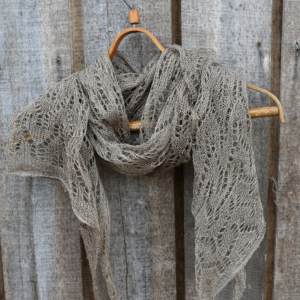 Knitted shawl draped over a wooden hanger against a rustic wooden background