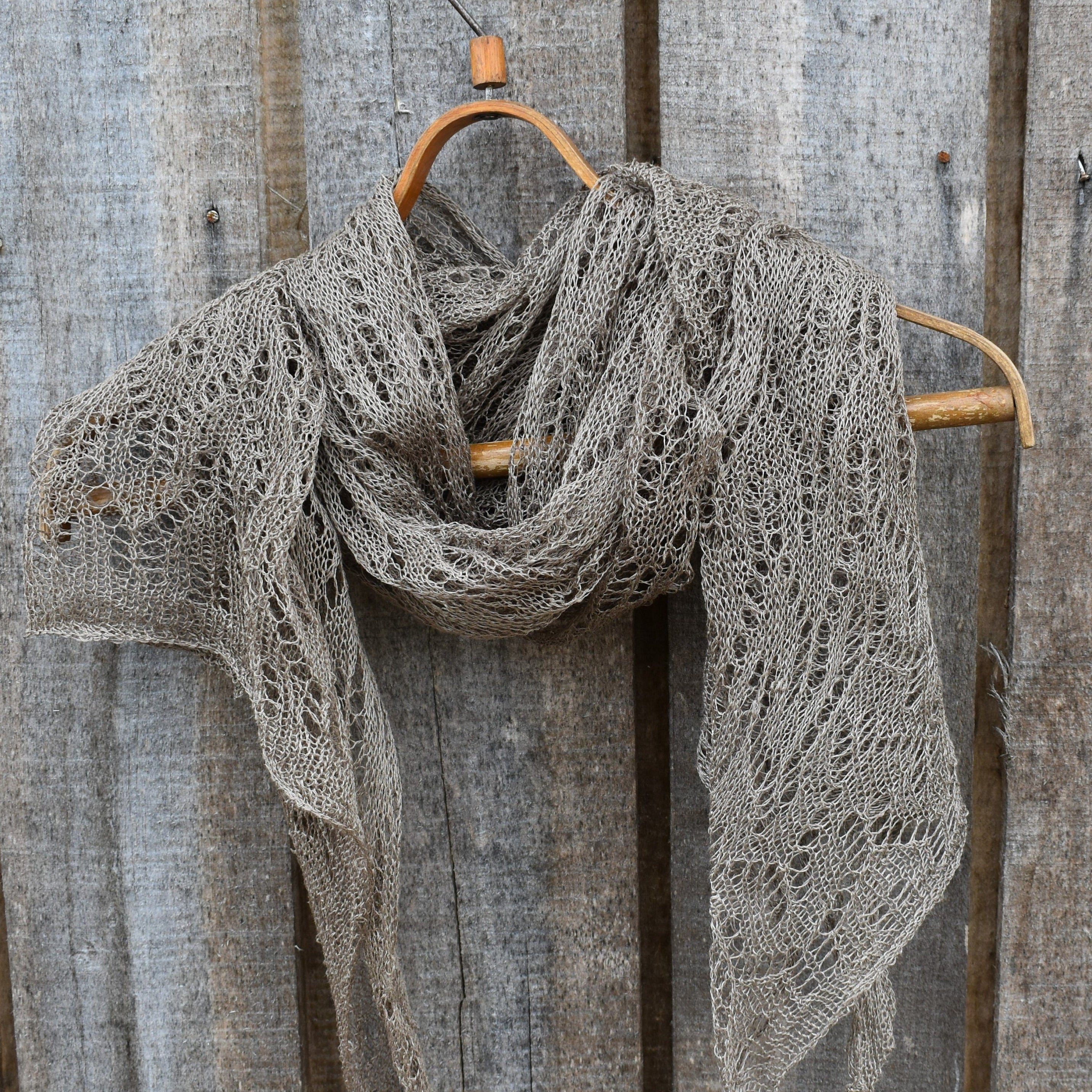 Knitted shawl draped over a wooden hanger against a rustic wooden background