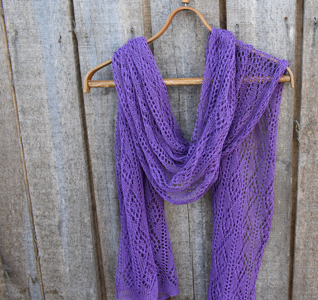 Purple knitted scarf on a wooden hanger against a rustic wooden background