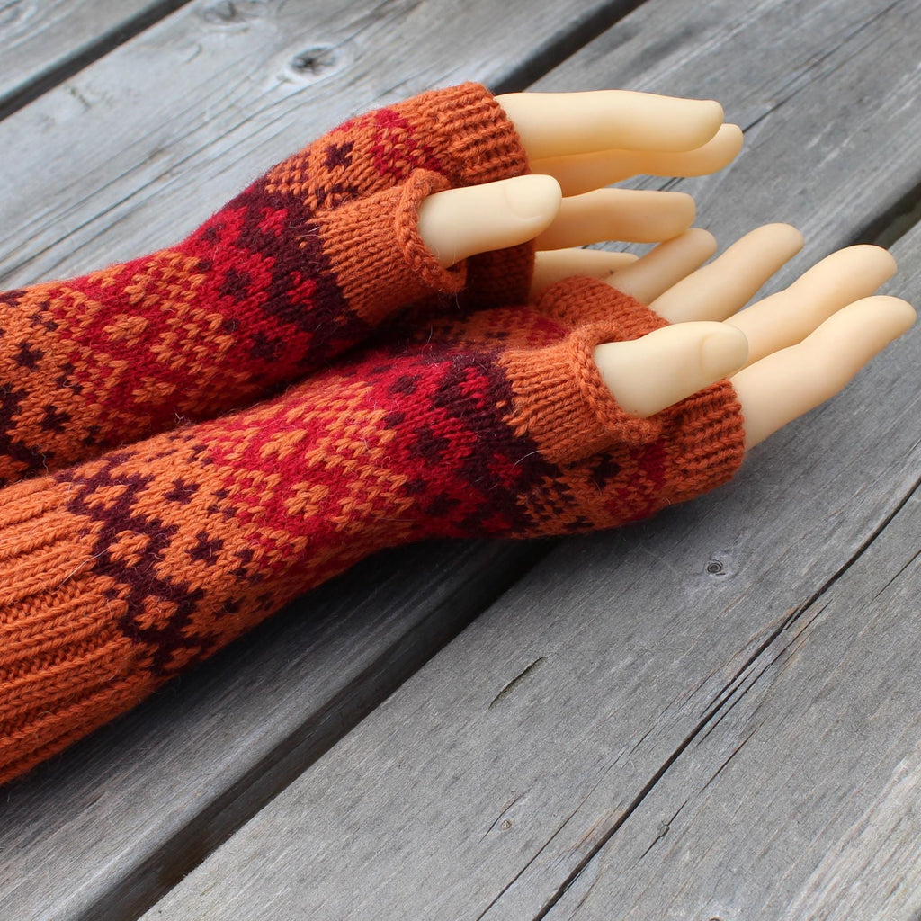Pair of orange and red patterned fingerless gloves on a wooden surface