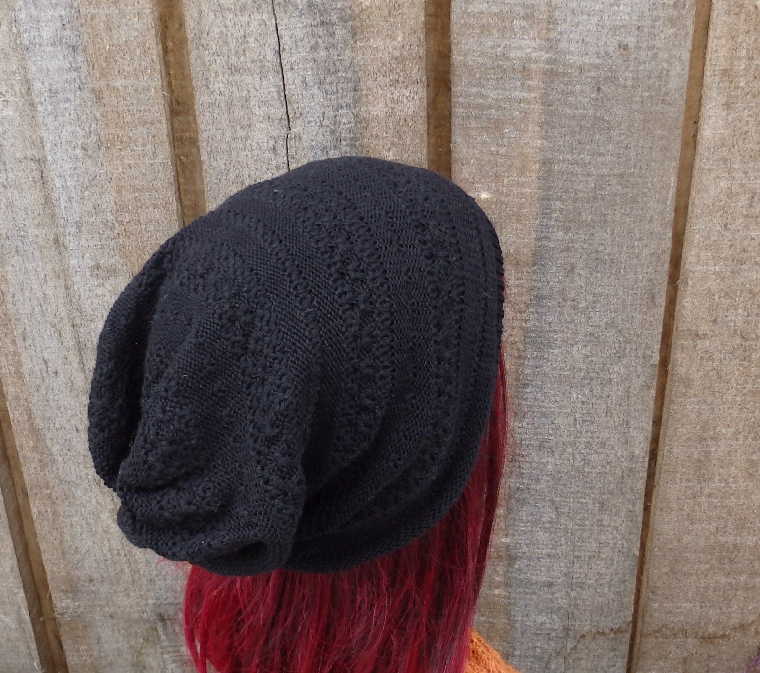 Black knit beanie on a mannequin head with red hair against a wooden panel background
