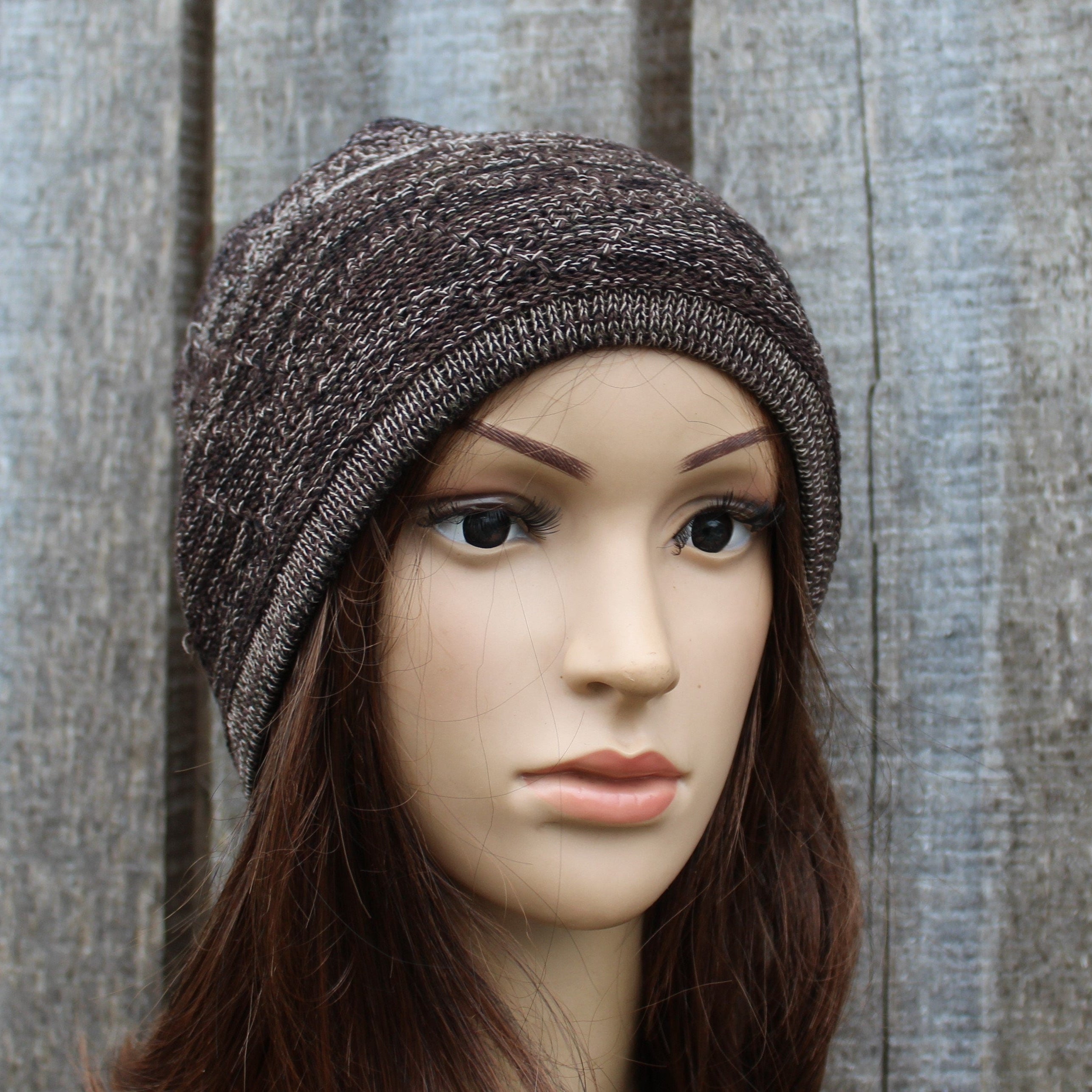 Mannequin head wearing a brown knit beanie against a wooden background