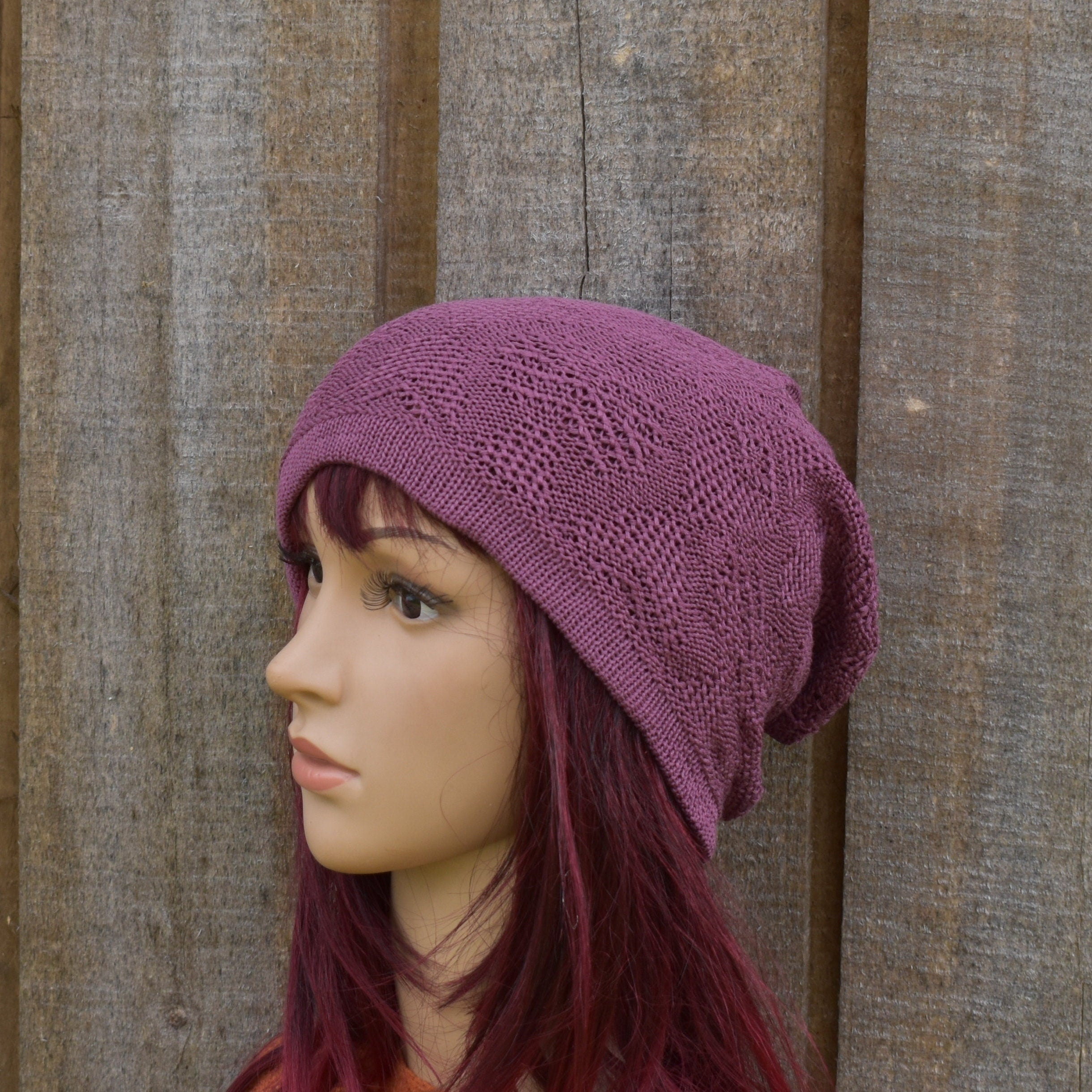 Mannequin head wearing a purple knitted hat against a wooden background