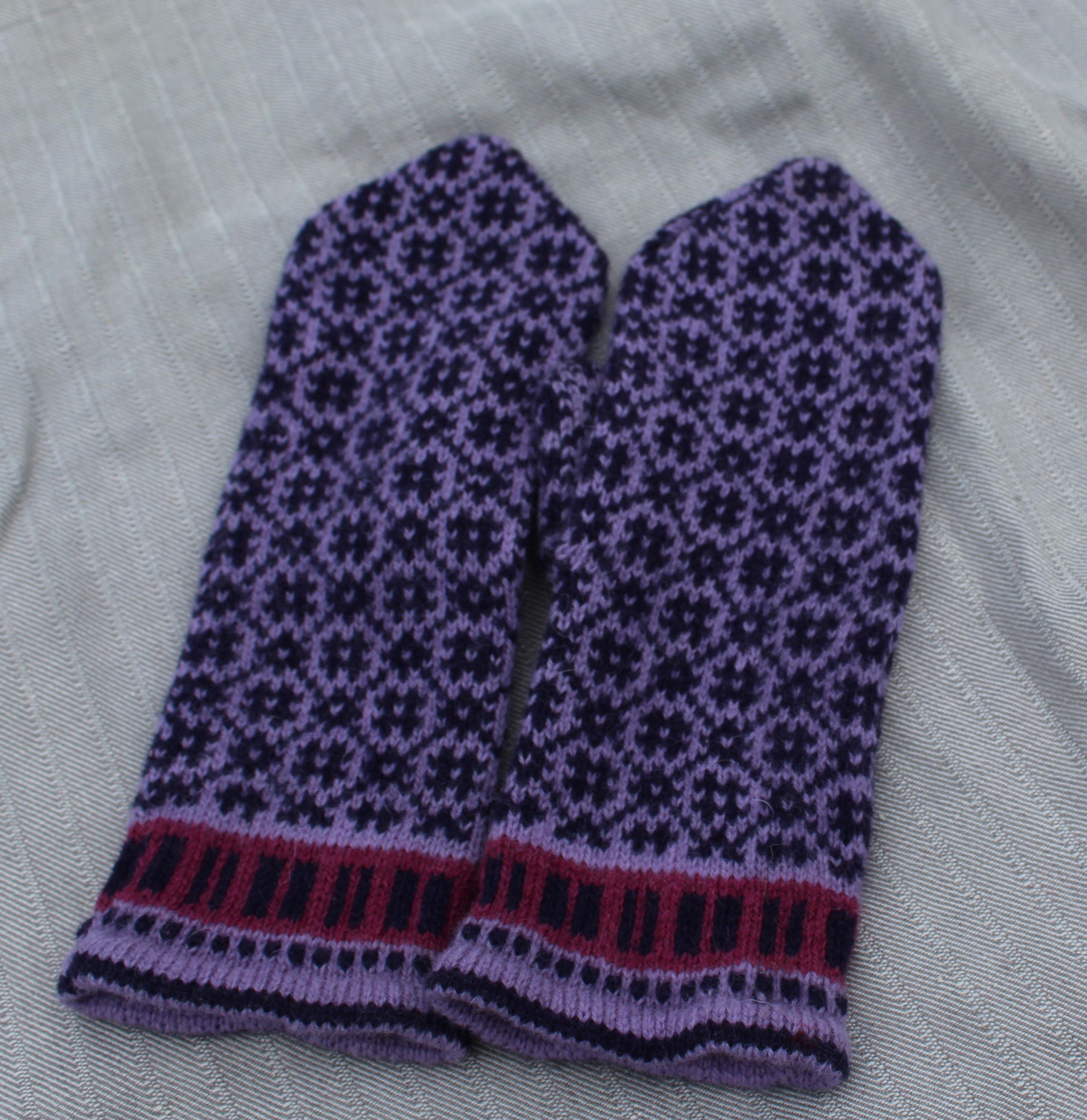 Pair of purple knitted mittens with a geometric pattern on a light gray background