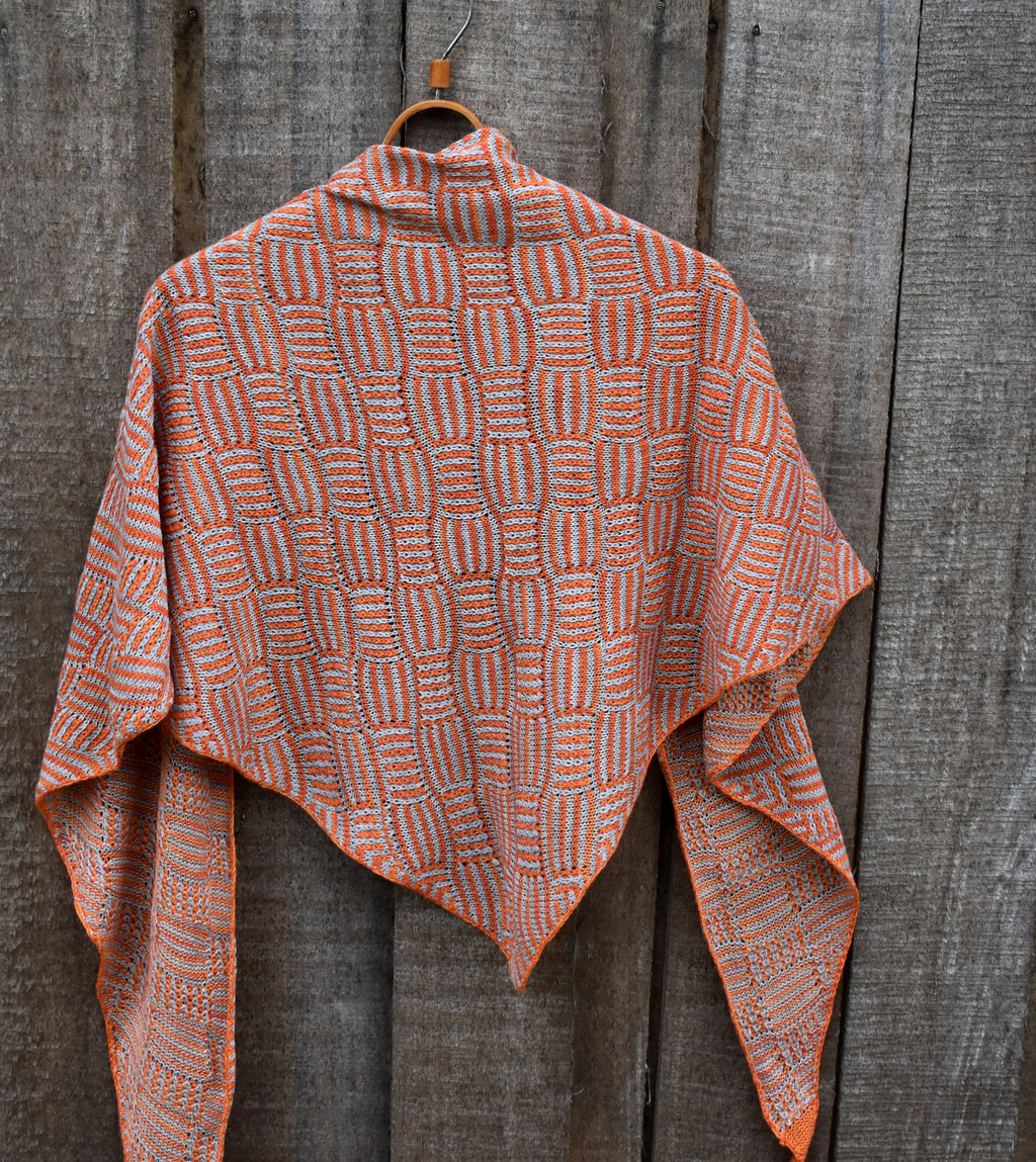 Knitted shawl with a geometric pattern hanging on a wooden surface