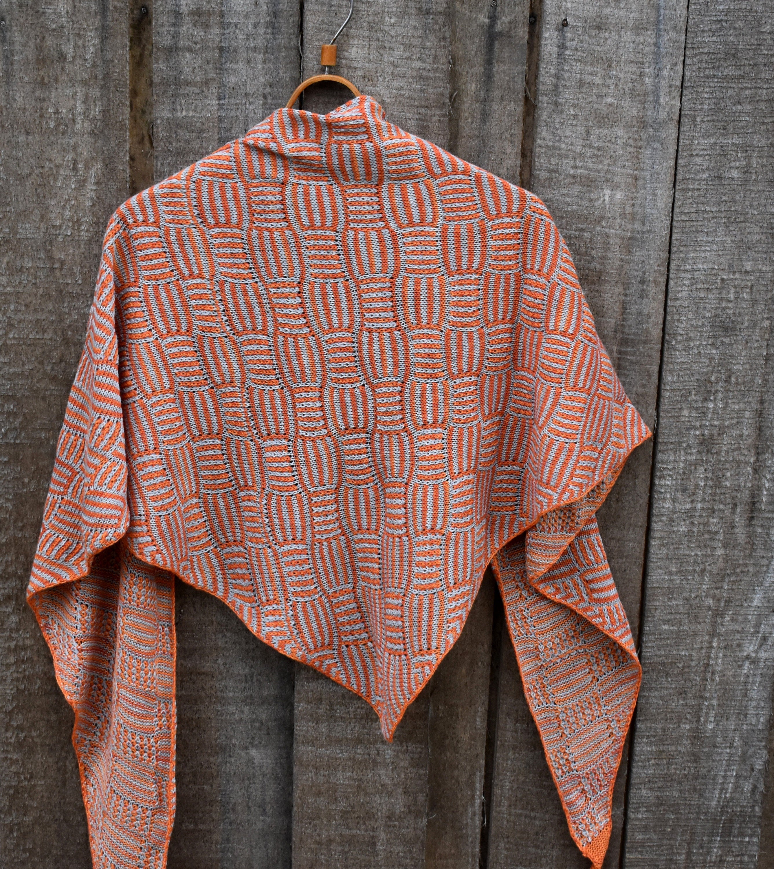 Knitted shawl with a geometric pattern hanging on a wooden surface