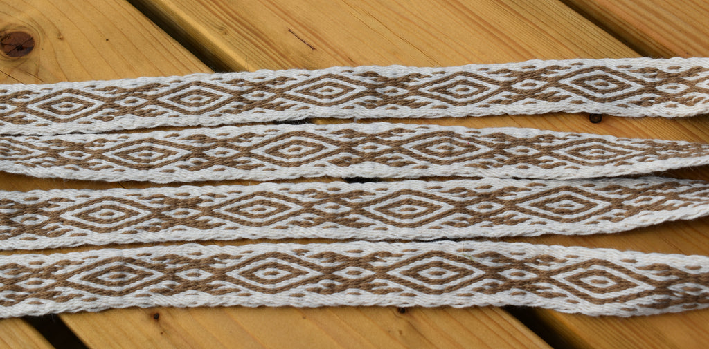 White braided elastic trim with a brown geometric diamond pattern, laid flat on a light brown wooden surface.
