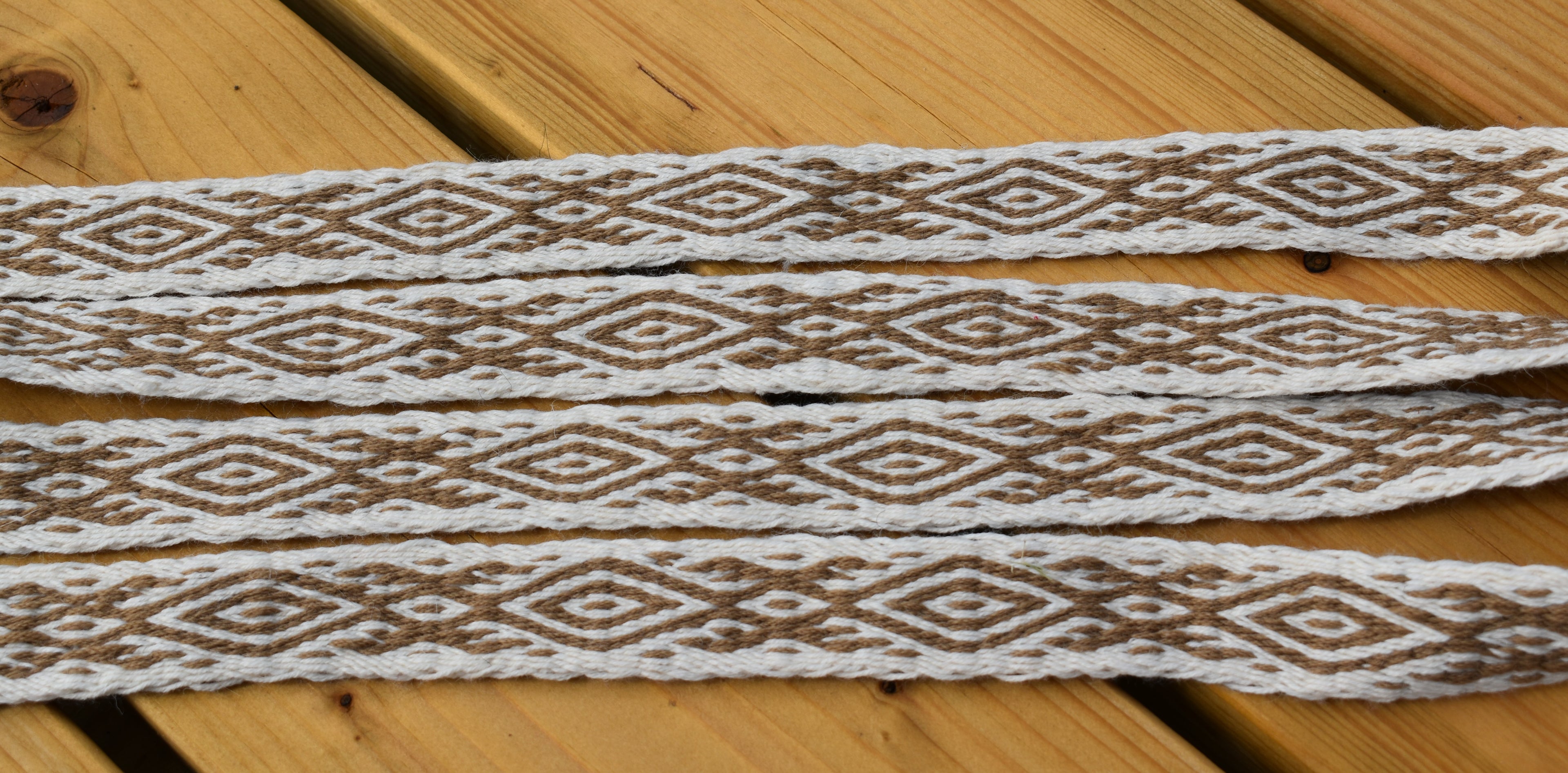 White braided elastic trim with a brown geometric diamond pattern, laid flat on a light brown wooden surface.