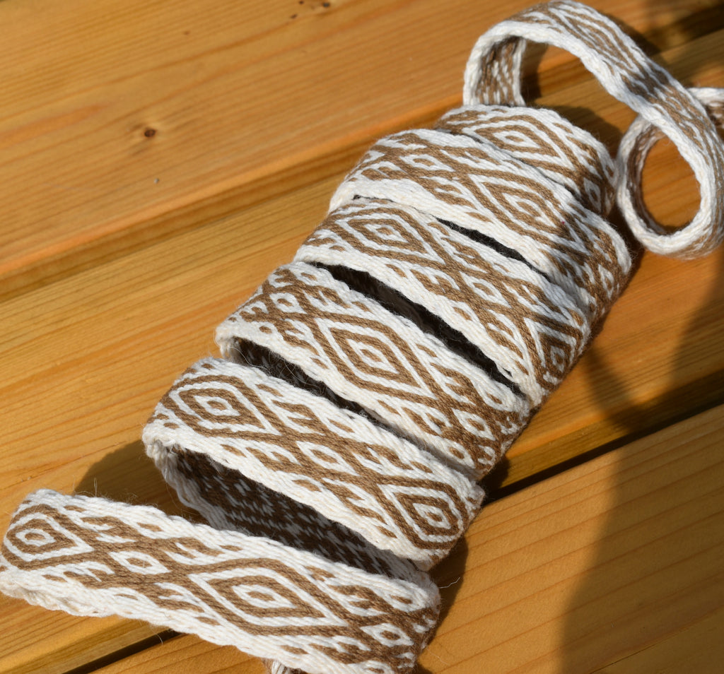 A roll of braided rope or twine with a brown and white geometric diamond pattern, shown on a wooden surface.