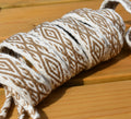 A close-up of a rolled piece of braided twine or cord with a geometric diamond pattern in brown and off-white, resting on a light wood surface.