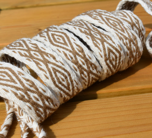A close-up of a rolled piece of braided twine or cord with a geometric diamond pattern in brown and off-white, resting on a light wood surface.