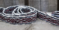 A close-up of a woven strap or belt with a geometric pattern in white, black, and dark red, resting on a rustic wooden surface.