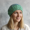 Woman wearing a green crocheted beanie against a gray background