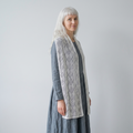 Woman wearing a long, light-colored cardigan over a gray dress against a plain background