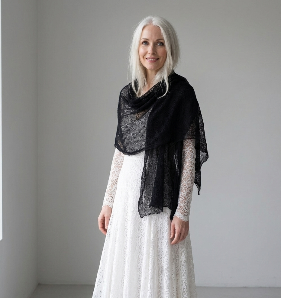 Woman wearing a black shawl over a white dress against a plain background