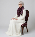 Woman wearing a white dress and purple patterned shawl sitting on a chair against a plain background