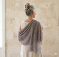 Woman wearing a gray knitted shawl against a beige wall