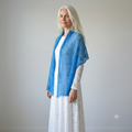 Woman wearing a blue shawl over a white dress against a plain background