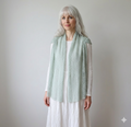 Woman wearing a light green knitted cardigan over a white dress against a plain background
