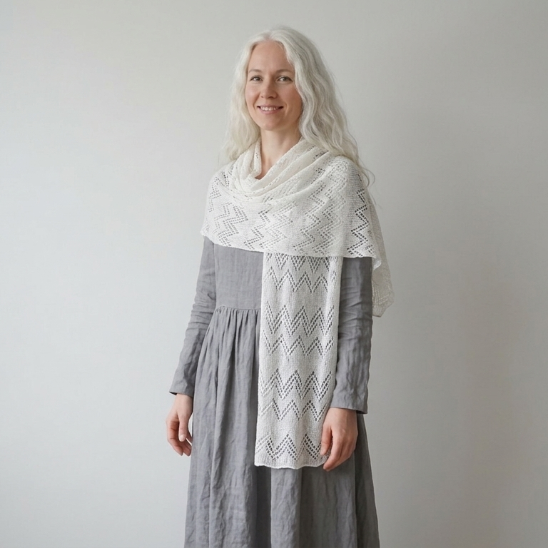Woman wearing a gray dress with a white patterned shawl against a plain background