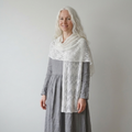 Woman wearing a gray dress with a white patterned shawl against a plain background
