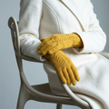 Person wearing mustard yellow gloves and a white coat, sitting on a chair with a neutral background