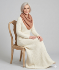 Woman wearing a white knitted dress and pink scarf sitting on a wooden chair against a gray background