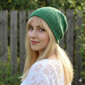 Woman wearing a green knitted beanie outdoors with a wooden fence and greenery in the background