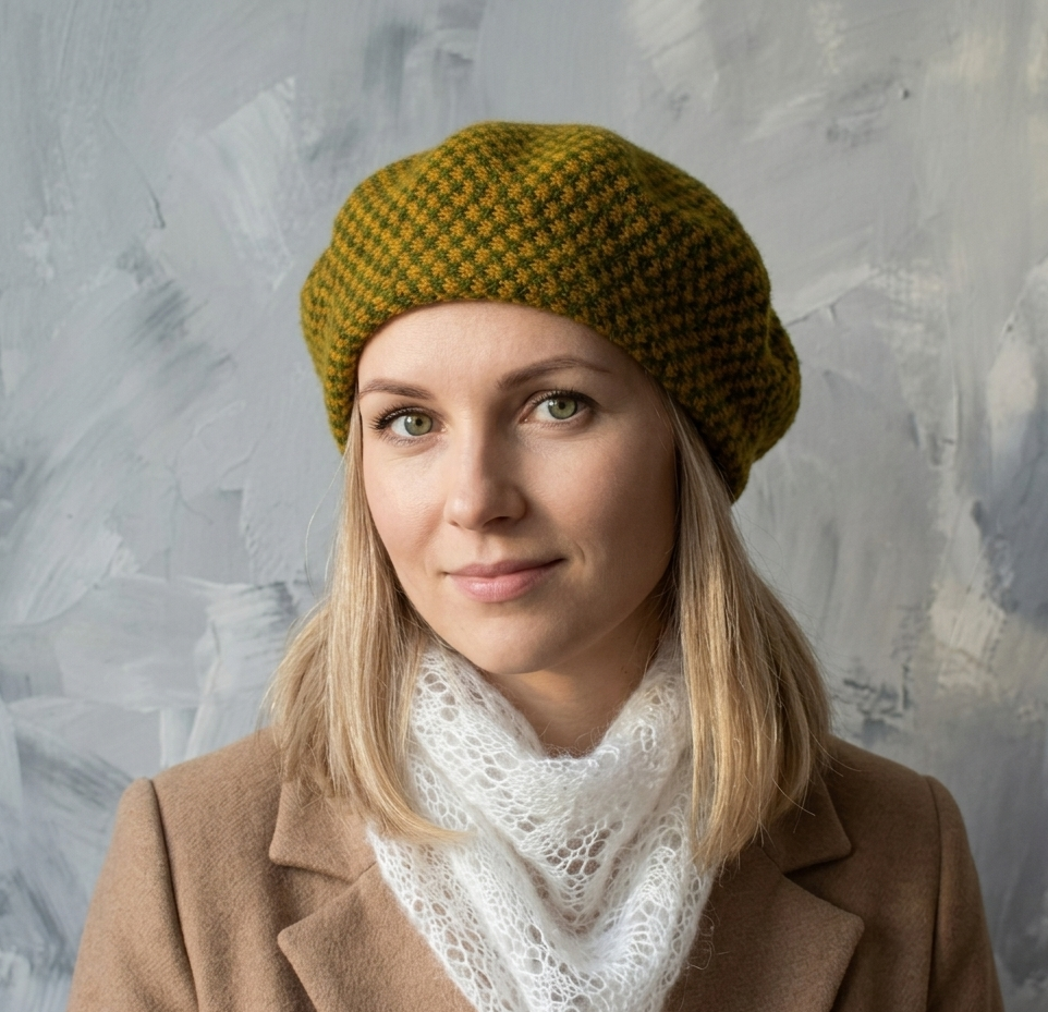 Woman wearing a green knitted hat and brown coat against a textured gray background