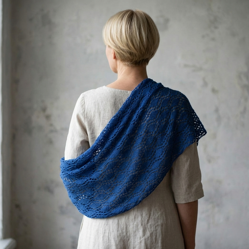 Person wearing a blue knitted shawl over a plain garment against a neutral background