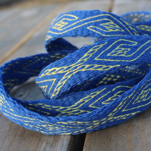 A close-up of a blue braided cord or strap with yellow geometric woven patterns, resting on a rustic wooden surface.