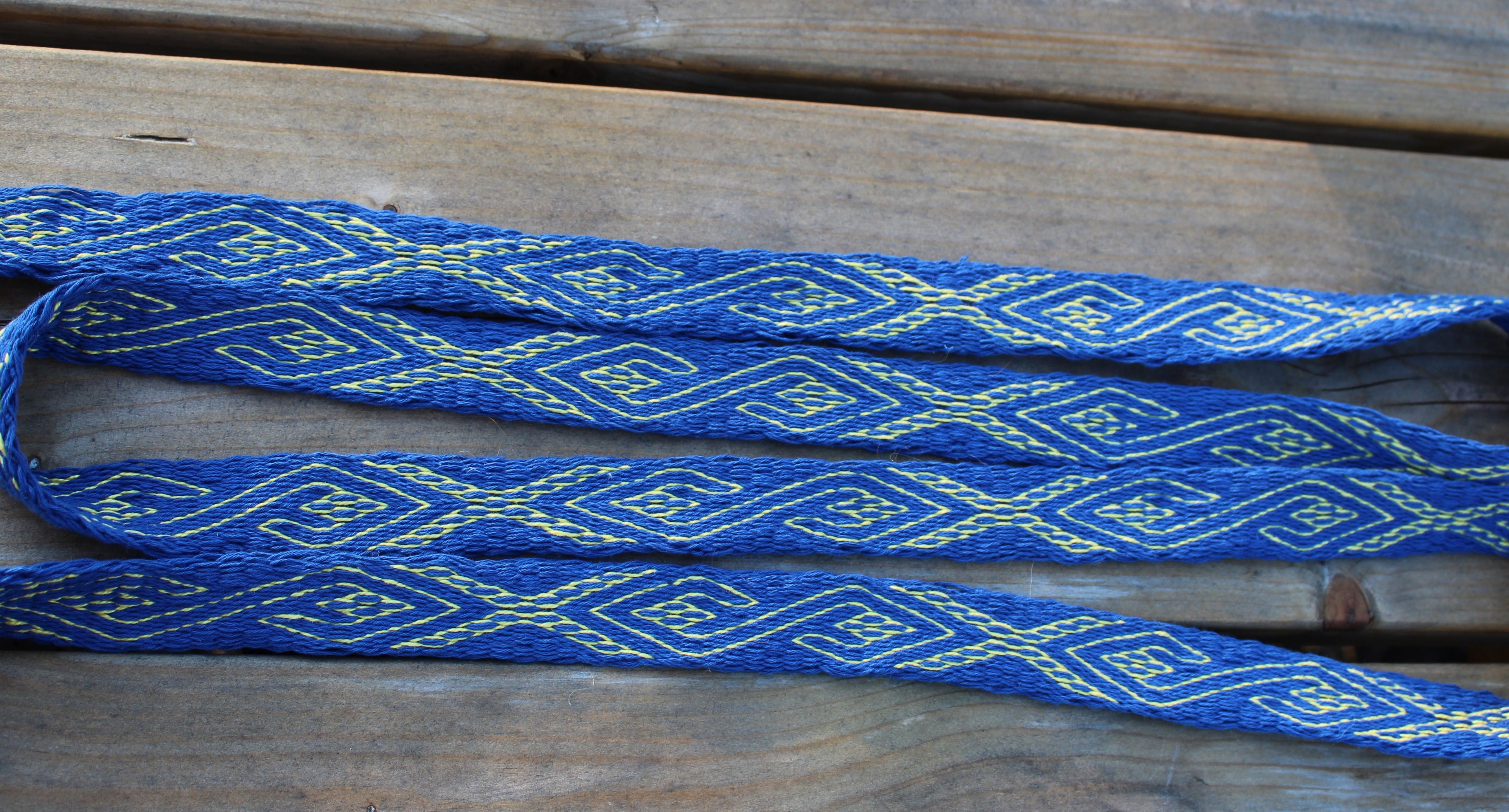 A blue woven strap with a repeating yellow geometric pattern, laid out on a rustic wooden surface.