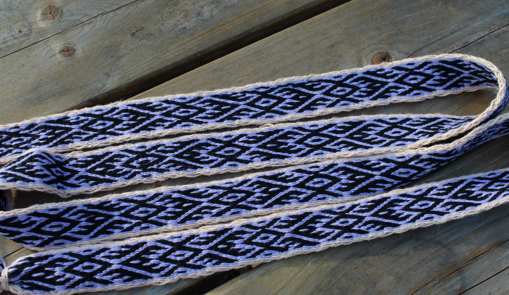 A close-up of a woven strap with a black and white geometric pattern, laid diagonally across weathered wooden planks.