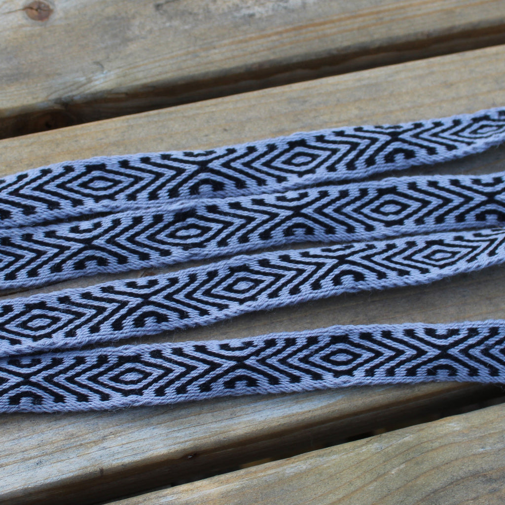 A woven strap with a black and gray geometric diamond pattern, laid out on a rustic wooden surface.
