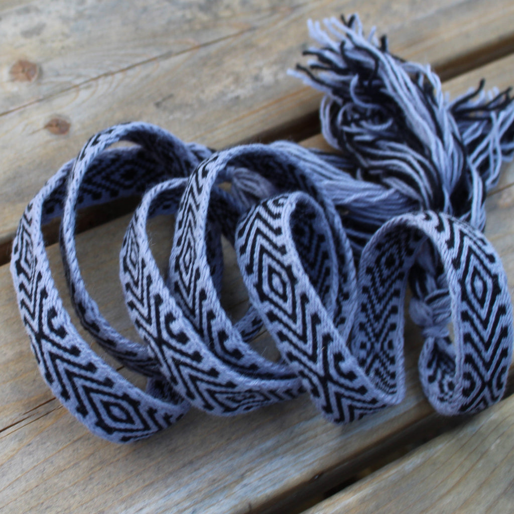 A black and white geometric patterned woven belt or strap, coiled on a rustic wooden plank surface.