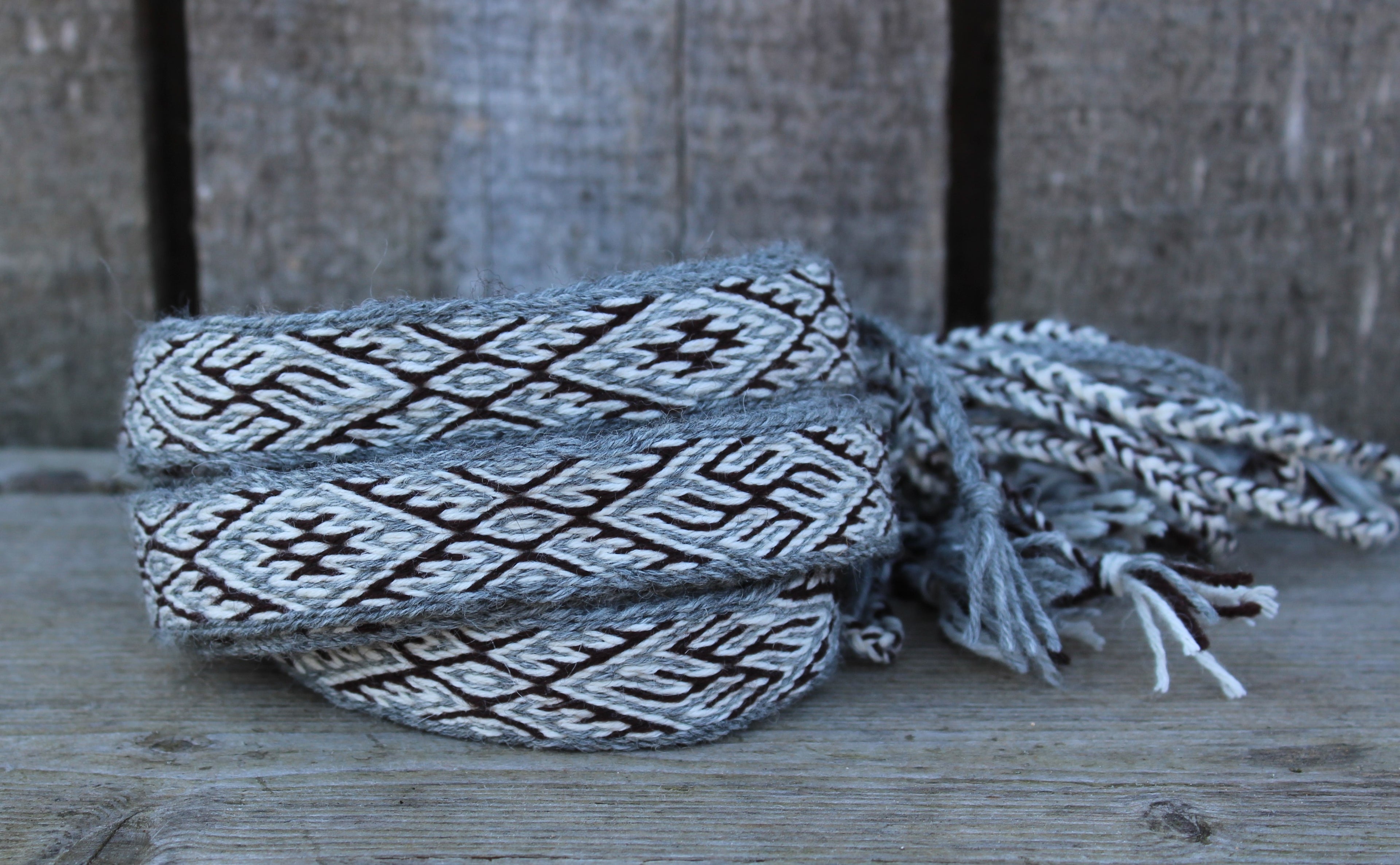 A woven gray and black textile wrap with geometric patterns and frayed ends, resting on a rustic wooden surface.