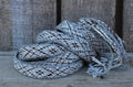 A coiled woven strap or belt with a gray, white, and black geometric pattern, resting on a rustic wooden surface against a weathered wood plank background.