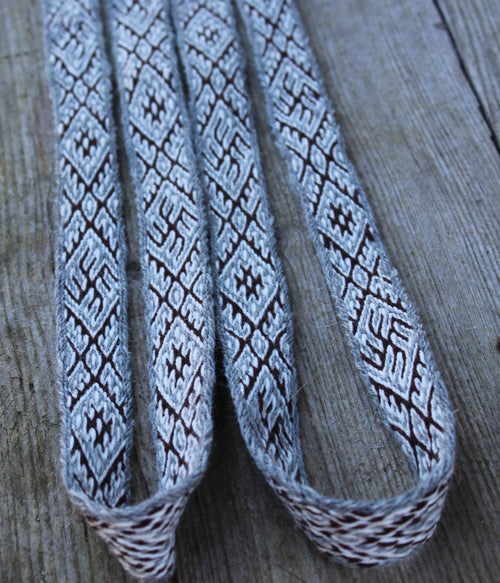 A close-up of a woven gray and white textile strap with a repeating geometric pattern, laid on a weathered wood surface.