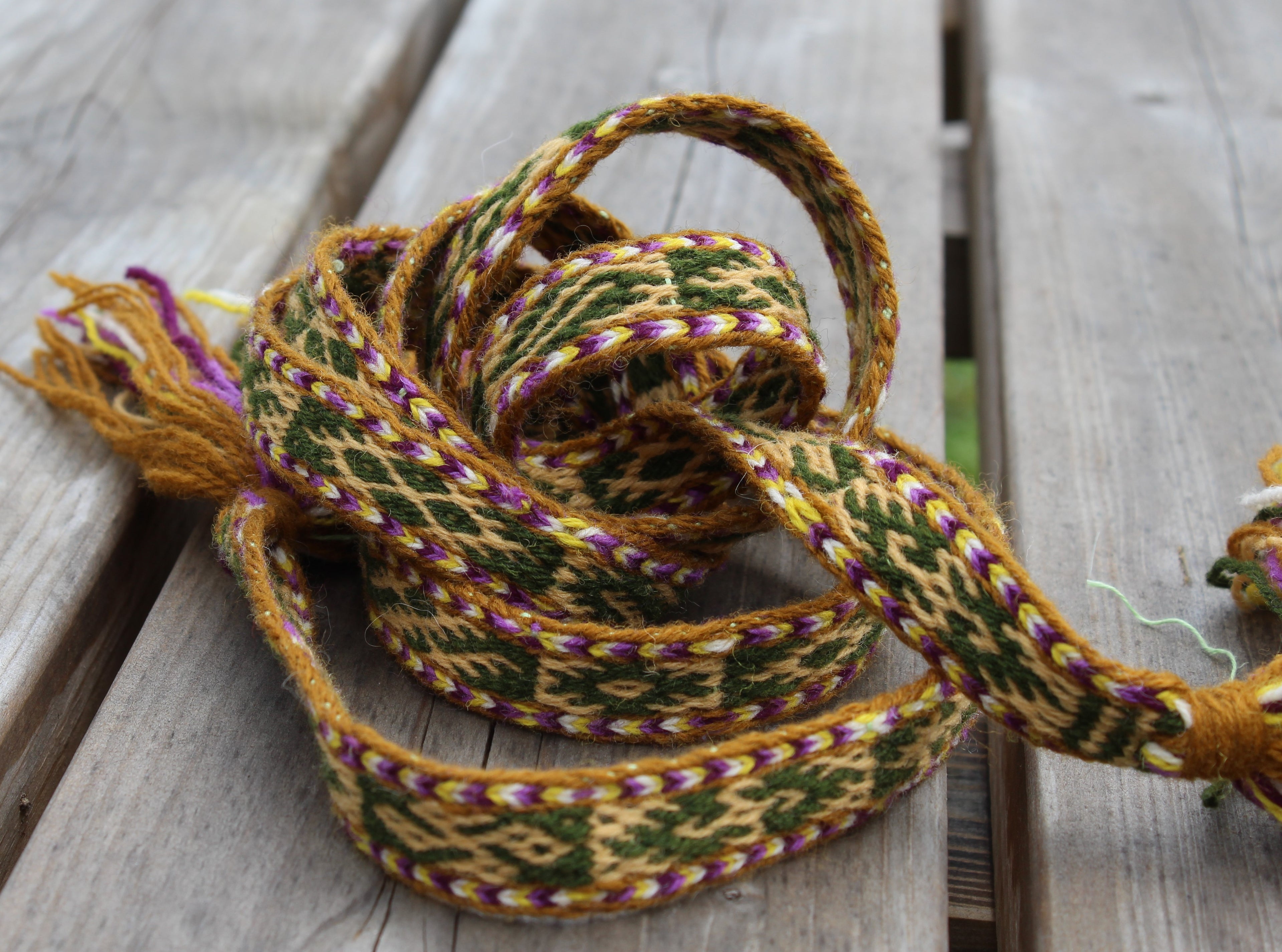 A coiled multicolor woven strap with purple tassels, resting on a weathered gray wooden surface.