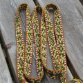 A close-up of a woven strap or belt with a geometric pattern in green, yellow, and purple, laid out on weathered gray wooden planks.
