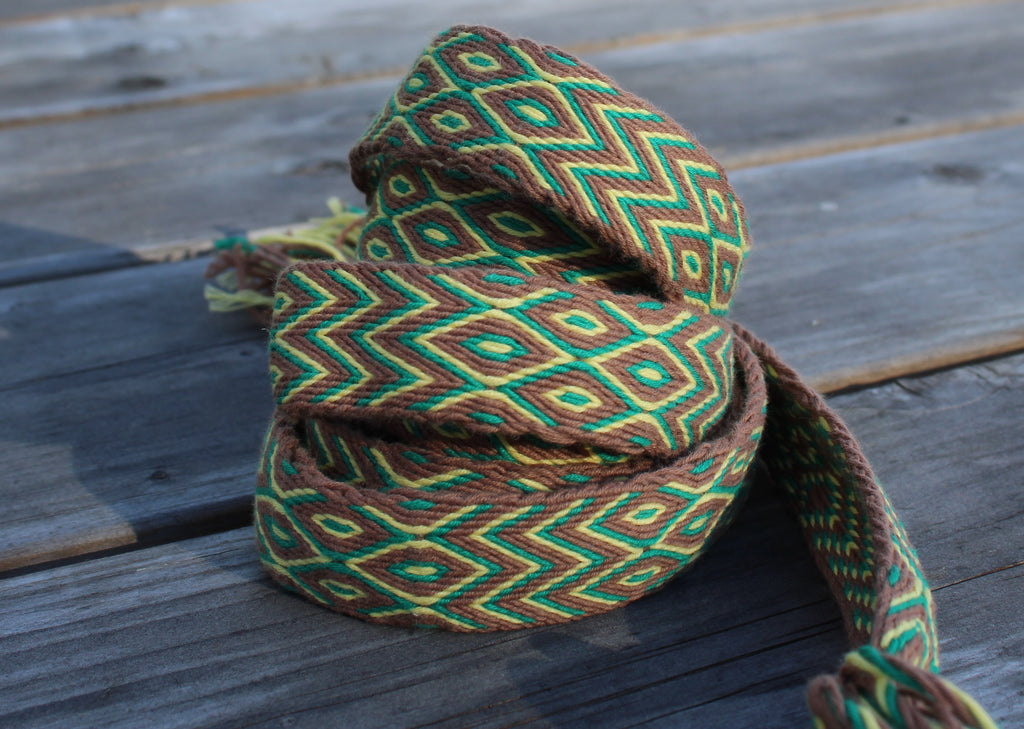 A coiled woven rope or strap with a geometric diamond pattern in green, brown, and yellow, resting on weathered wooden planks.