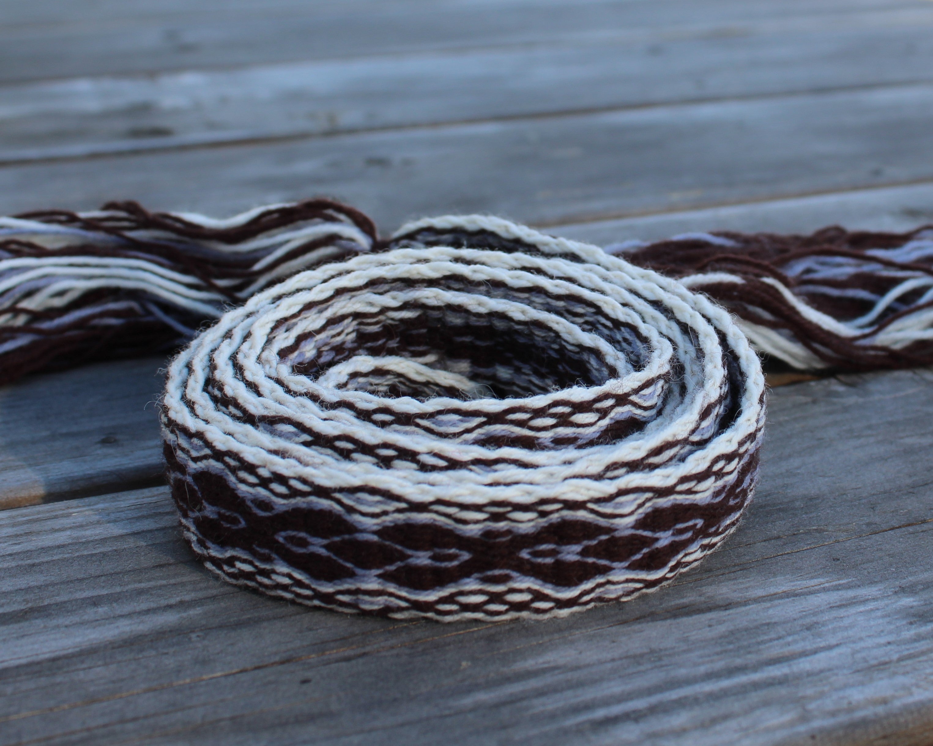 A coiled piece of thick braided cord or strap in a brown and off-white pattern, resting on a weathered gray wooden surface.